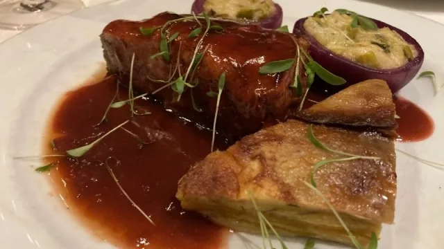 Solomillo de cerdo relleno de damascos y panceta, acompañado con mil hojas de batata y cebolla rellena, aliñado con salda de oporto.