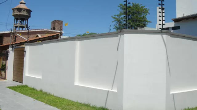 Sobre una tapia: las ménsulas que soportan los cables de acero y aisladores son amuradas por medio de tarugos y tirafondos.