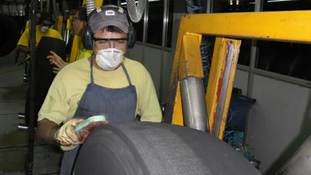Operarios raspan la superficie del neumático para luego colocar caucho vulcanizado en la superficie y adherir una nueva banda.